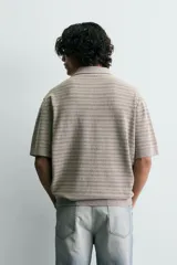 Polo relaxed fit de punto tejido en hilatura con mezcla de algodón y textura rizada, color gris con diseño a rayas sutiles, cuello solapa con cierre frontal de botonadura y manga corta con acabados en rib.