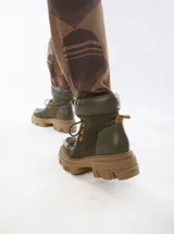 Borcegos de caña baja con diseño robusto, confeccionados en una combinación de gamuza y cuero sintético en tonos verde oliva. Presentan suela track de goma dentada en color suela, cordones al tono con ojalillos amarillos y cuello acolchado para mayor confort.