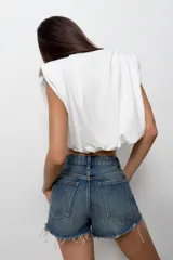 Top de algodón con cuello redondo, diseño sin mangas con hombreras marcadas y detalle de pliegues. Presenta un bajo acabado tipo globo con elástico.