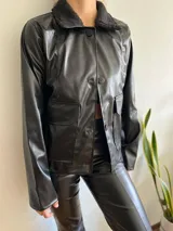 Chaqueta negra de cuero sintético con cuello de piel sintética, cierre frontal con botones, bolsillos delanteros con solapa y corte recto.
