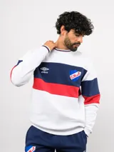 Buzo de cuello redondo confeccionado en felpa, con diseño de bloques de color en azul, rojo y blanco. Presenta el logo de Umbro y el escudo del Club Nacional de Football bordados en el frente.