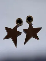 Caravanas colgantes con base redonda de resina negra rodeada de strass dorado, y dije en forma de estrella de acrílico espejado color cobre.