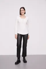 Remera blanca de manga larga, entallada, con cuello redondo y una hilera de botones en el frente. Incluye un pequeño bolsillo decorativo en el pecho.