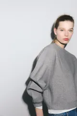 Sudadera gris de cuello redondo y manga larga, con puños y dobladillo acanalados.