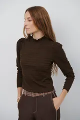 Polera de manga larga con cuello alto y detalle de volados en el borde. Confeccionada en tejido acanalado de textura suave y ajuste al cuerpo.