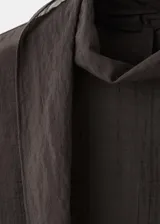 Blusa de color marrón oscuro con textura, cuello alto envolvente con detalle de fular integrado, manga larga con puños abotonados y diseño recto.