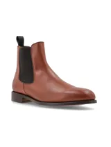 Bota tipo Chelsea de cuero color marrón, con paneles laterales elásticos en color negro y tirador en la parte trasera. Presenta una suela plana con pequeño tacón.