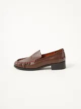 Mocasines de cuero negro con costuras pespunteadas en hilo blanco a contraste, diseño fruncido en la puntera, talón plano con pequeño tacón y apliques sutiles en charol.