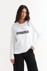 Remera de manga larga color beige con cuello redondo a la base. Presenta un estampado frontal con un dibujo de labios en color fucsia y la palabra 'BESITO' en color negro.