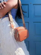 Bandolera de símil cuero color verde oliva, con diseño de dos compartimentos con cierre y correa ajustable de tela con patrón geométrico.