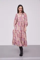 Vestido midi de viscosa con estampado patchwork en tonos rosados y violetas. Presenta cuello redondo con cordones ajustables, mangas 3/4 abullonadas y diseño holgado con falda de volados.