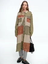 Vestido camisero de corte midi con diseño patchwork que combina paneles en tonos crudo y marrón con estampados florales sutiles. Presenta cierre frontal con botones, cuello camisero y mangas largas con puños.