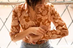 Camisa de corte clásico con cuello camisero y cierre frontal de botones, manga larga con puños abotonados, confeccionada en tela con estampado floreado en tonos camel y rosa.