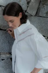 Camisa de algodón color beige con detalles de encaje y broderie en el canesú y las mangas. Presenta cuello camisero, cierre frontal con botones y mangas largas con puños.