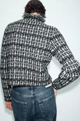 Chaqueta de punto con textura, cuello redondo y manga larga. Presenta detalles de acabados deshilachados en los bordes y cierre frontal con ganchos.