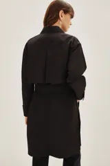Trench negro de corte midi con cuello camisero, cierre frontal y cinturón ajustable a la cintura. Presenta mangas largas con puños rectos y un diseño minimalista y versátil.