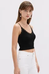 Musculosa de punto blanco, corte crop, con tirantes finos, escote en V adornado con detalles de encaje y un pequeño lazo en el centro.