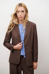 Blazer de corte sastrero en color gris oscuro, con cierre frontal de un botón, solapas clásicas y bolsillos con solapa. Presenta una estructura entallada y hombreras marcadas.