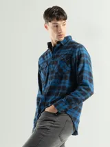 Camisa de franela a cuadros color celeste, gris y negro, de manga larga con dos bolsillos frontales con solapa abotonada.