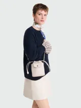 Bolso pequeño tipo saco (bucket bag) de cuero color beige claro, con cierre de solapa y broche a presión. Posee cordones ajustables laterales y correa fina para llevar cruzado.