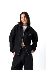 Camisa de gabardina negra de diseño unisex y corte holgado. Cuenta con un cierre frontal de doble camino, cuello camisero y detalles de estampa y bordado en el pecho con el texto 'Low Profile'.