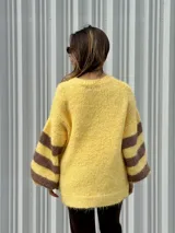 Buzo de tejido de punto con textura peluda, de corte holgado y mangas amplias. Presenta un diseño geométrico con una flor grande estampada en el centro, combinando tonos fucsia, rosa y marrón en un patrón de bloques y rayas.