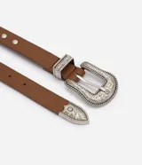 Cinturón de estilo western confeccionado en poliuretano color marrón. Presenta hebilla metálica grande con grabados ornamentales, puntera metálica decorada, pasador con relieve y aplicaciones metálicas circulares a lo largo de la tira.