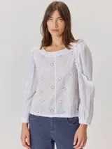 Camisa blanca de algodón con mangas largas abullonadas, detalle de volados en los hombros y puños elásticos. Presenta un diseño con cuello redondo y corte holgado.