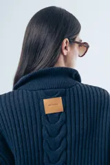 Sweater de punto grueso color azul marino, con cuello polo y cierre frontal parcial. Presenta un diseño de tejido trenzado en el centro y mangas largas con puños acanalados.