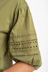Remera de algodón color crudo con cuello redondo y mangas abullonadas de largo 3/4. Las mangas presentan detalles de encaje bordado y perforado con terminación elástica.