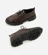 Mocasín tipo dockside color marrón oscuro con acabado texturizado, ajuste frontal con cordones y suela track robusta de goma.
