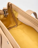 Cartera tipo tote de símil cuero color beige, con doble asa de mano, correa ajustable y desmontable, y llavero colgante en forma de corazón. Cuenta con detalle de logo metálico en el frente y broche a presión.