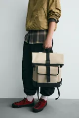 Mochila verde militar con acabado engomado, solapa superior con cierre de hebilla y cremallera, bolsillo frontal con cierre imantado, compartimento interno para laptop de hasta 13 pulgadas, asa de mano superior, correas de hombro ajustables y espalda acolchada. Base de cuero sintético negro.