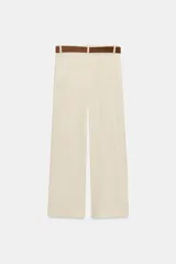 Pantalón culotte de tiro alto color beige, confeccionado con lino. Presenta pernera ancha y corta, bolsillos delanteros y falsos bolsillos de vivo en la espalda. Incluye un cinturón marrón con hebilla metálica redonda y cierre frontal con cremallera, botón interior y gancho.
