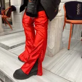 Pantalón de cuero sintético rojo con acabado metalizado, corte flare y aberturas laterales en los bajos con broches a presión.