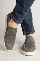 Zapatillas tipo mocasín de gamuza gris plomo con suela blanca de goma y detalle de antifaz en el empeine.