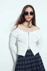 Top de punto acanalado negro, con diseño off-shoulder y escote amplio. Presenta mangas largas y cierre frontal completo con doble cursor, permitiendo ajustar la apertura superior e inferior.