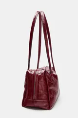 Bolso de hombro de piel con formato bowling, acabado texturizado tipo cocodrilo y color bordó. Cuenta con doble asa de hombro, cierre principal de cremallera con doble tirador y bolsillo interior con cremallera.