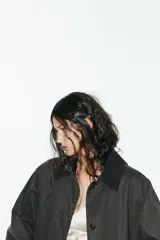 Gabardina larga color gris oscuro con efecto encerado, cuello solapa de pana, manga larga, bolsillos laterales con solapa y cierre frontal con botones ocultos.