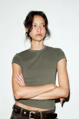 Camiseta de corte entallado confeccionada en mezcla de algodón, con cuello redondo y mangas cortas. Presenta un diseño básico de bajo recto en color gris oscuro.