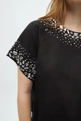 Blusa blanca de manga corta con cuello redondo y bordado de lentejuelas y mostacillas plateadas en el cuello y las mangas.