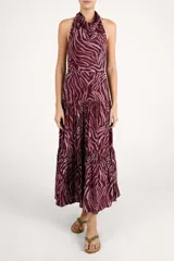 Vestido largo con escote halter y espalda descubierta, confeccionado en tela fluida con estampado animal print en tonos bordó y rosado. Presenta un corte entallado en la cintura y falda con volados escalonados.