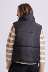 Chaleco de abrigo tipo puffer en color negro, con cuello alto, cierre frontal con cremallera y botones a presión.