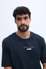 Remera oversize verde militar, confeccionada en 100% algodón, con cuello redondo y diseño relajado. Presenta un pequeño bordado frontal en tono naranja.