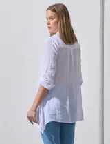 Camisa larga de rayón, con cuello camisero, cierre frontal de botones y mangas con presilla para regular el largo. Presenta un corte holgado con tajos laterales en el ruedo.