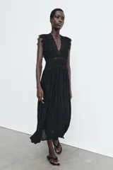 Vestido midi negro de escote pico y manga sisa, con detalles de bordados combinados a tono. Presenta un tejido plisado con efecto arrugado y cierre en la espalda con lazada y cremallera oculta.