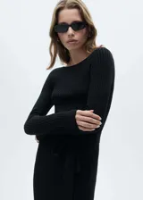 Vestido midi de punto acanalado en color negro, con diseño entallado, cuello barco y manga larga. Incluye un cinturón desmontable a tono y cuenta con una abertura lateral en el ruedo.