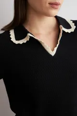 Sweater de punto negro de manga corta con cuello polo y ribetes contrastantes en color beige con detalles de encaje en el cuello y los puños.