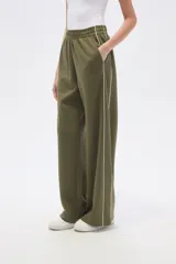 Pantalon deportivo de corte ancho y tiro alto, color verde oliva, con cintura elástica y una línea vertical blanca lateral en cada pierna.