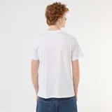 Remera blanca de manga corta y cuello redondo con diseño estampado frontal en tonos azules y verdes con gráficos y texto.